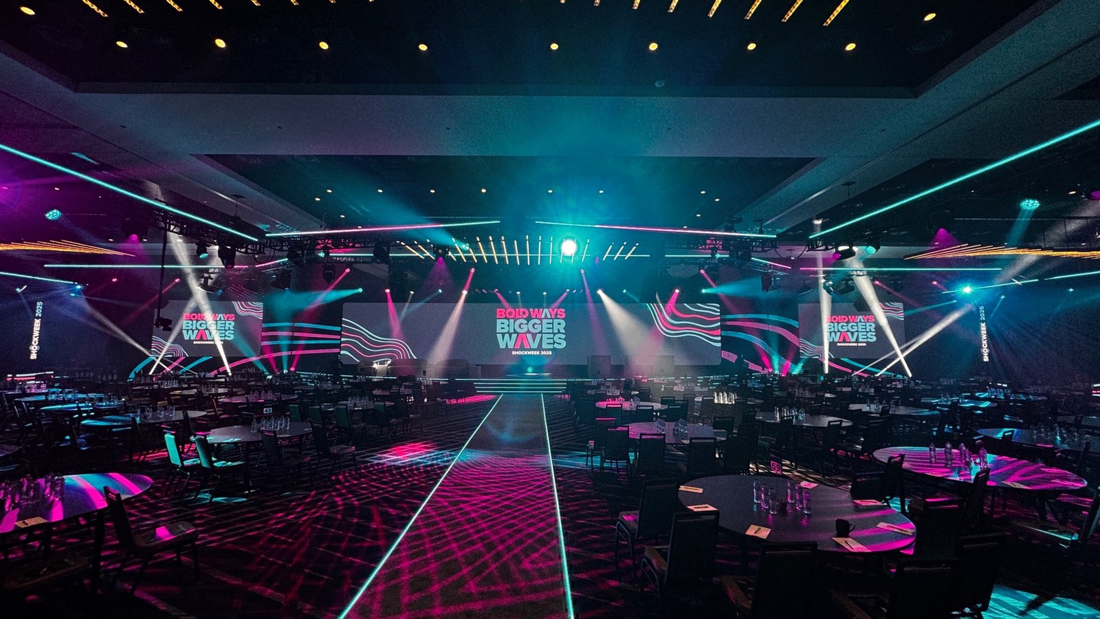 A corporate event room with audience seating, a central runway and a coordinated stage-lighting design.