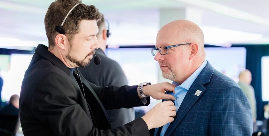 A production team member fitting a presenter with a microphone before going on stage.